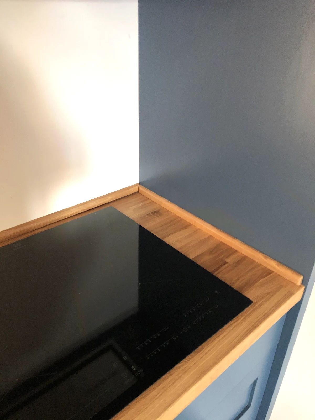 Detail rohu dubové pracovní desky s černou indukční varnou deskou v modré kuchyni